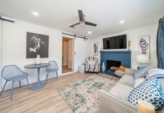 living room featuring ceiling fan, a fireplace, light hardwood / wood-style floors, and a barn door