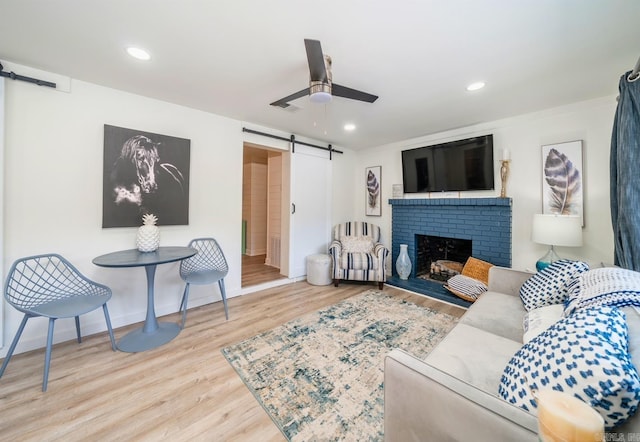 living area featuring a barn door, ceiling fan, wood finished floors, a brick fireplace, and recessed lighting