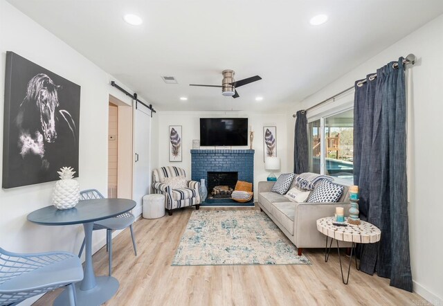 living room featuring a fireplace, ceiling fan, light hardwood / wood-style floors, and a barn door