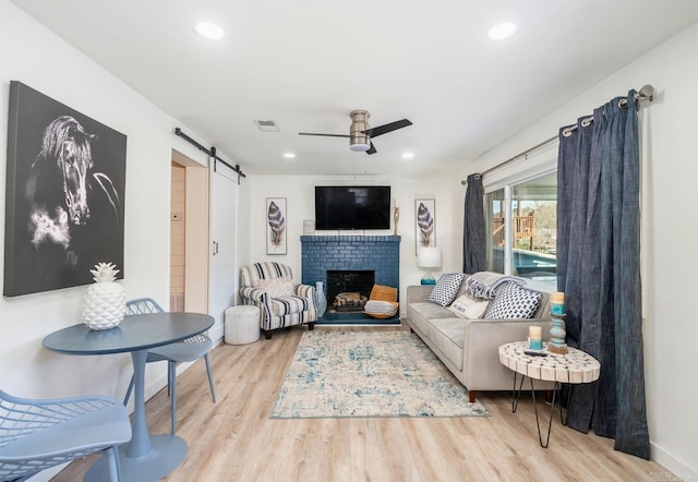 living room featuring a fireplace, visible vents, a barn door, a ceiling fan, and wood finished floors