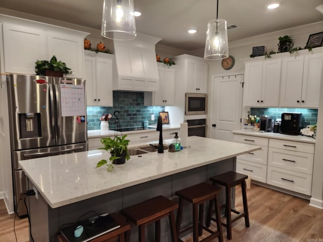 kitchen with a breakfast bar, tasteful backsplash, light wood-style flooring, appliances with stainless steel finishes, and white cabinetry