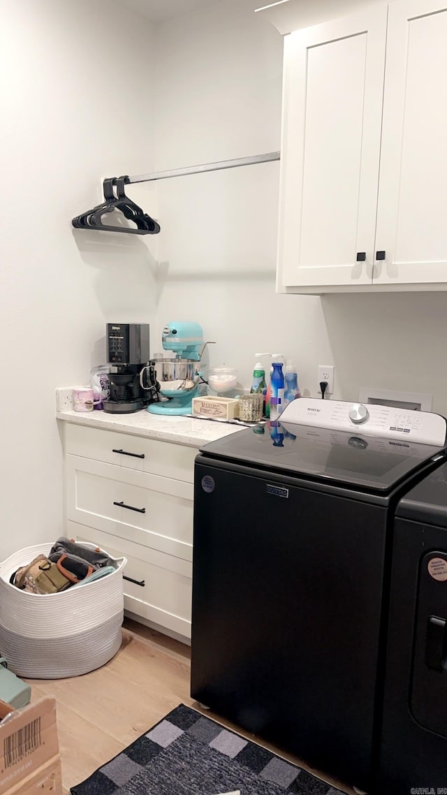 washroom featuring washing machine and dryer, cabinet space, and light wood-style floors