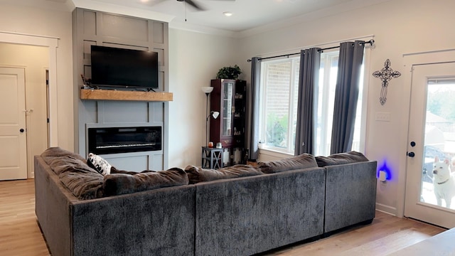 living room with light wood finished floors, ceiling fan, a fireplace, and ornamental molding