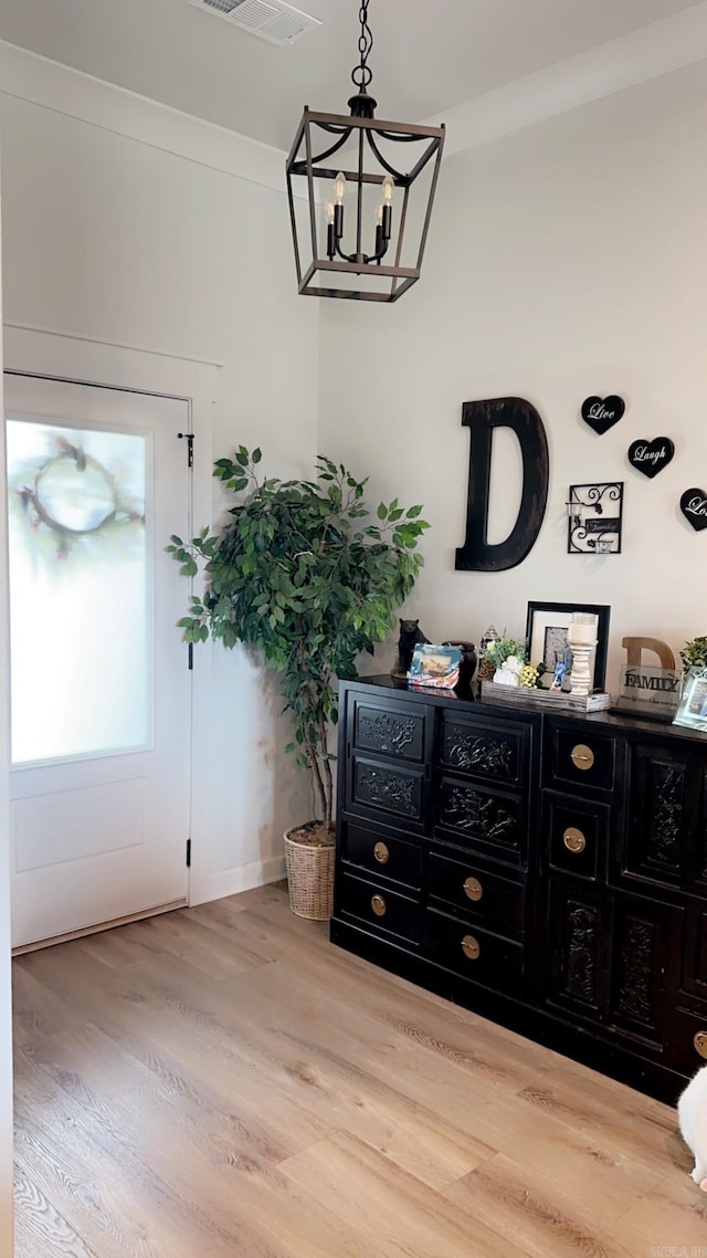 doorway to outside with visible vents, crown molding, an inviting chandelier, and wood finished floors