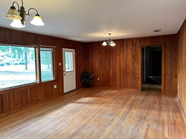 empty room with wood walls, a chandelier, and light hardwood / wood-style floors