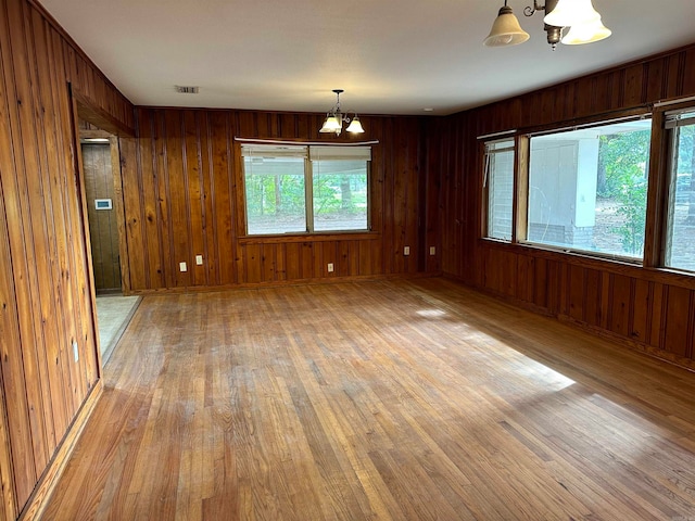 unfurnished room featuring wood walls, a notable chandelier, and light hardwood / wood-style flooring