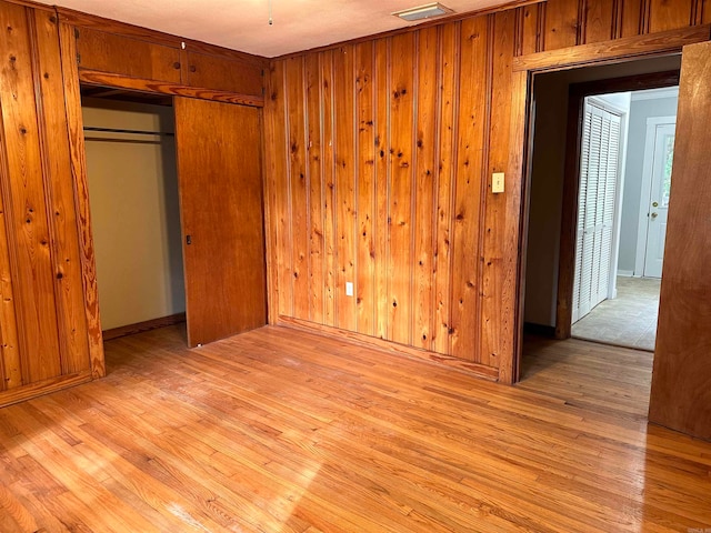 unfurnished bedroom featuring a closet, wood walls, and light hardwood / wood-style floors