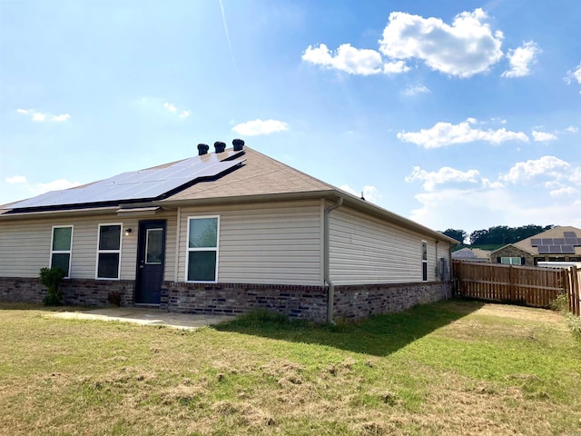 rear view of property featuring roof mounted solar panels, fence, a lawn, and brick siding