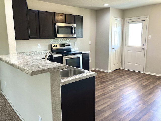 kitchen with stainless steel appliances, dark wood-type flooring, a peninsula, and baseboards