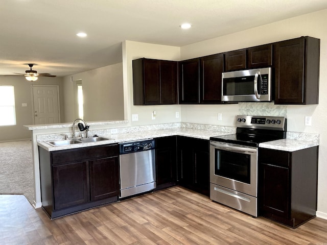 kitchen featuring recessed lighting, stainless steel appliances, a sink, dark brown cabinets, and light wood finished floors