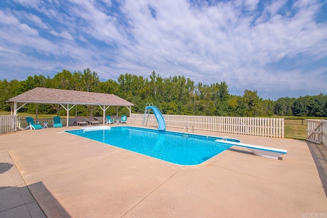 view of pool with a water slide, a diving board, and a patio area