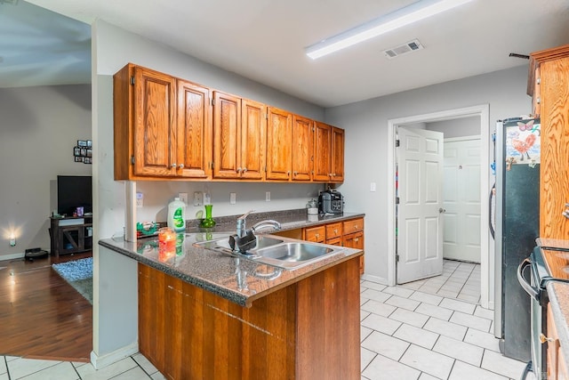 kitchen with a peninsula, a sink, visible vents, brown cabinets, and electric range oven