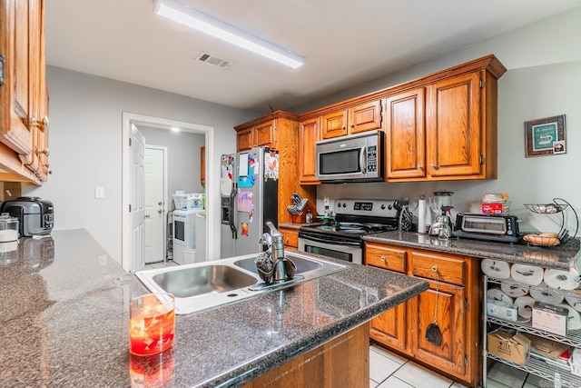 kitchen featuring light tile patterned flooring, stainless steel appliances, a sink, visible vents, and brown cabinetry