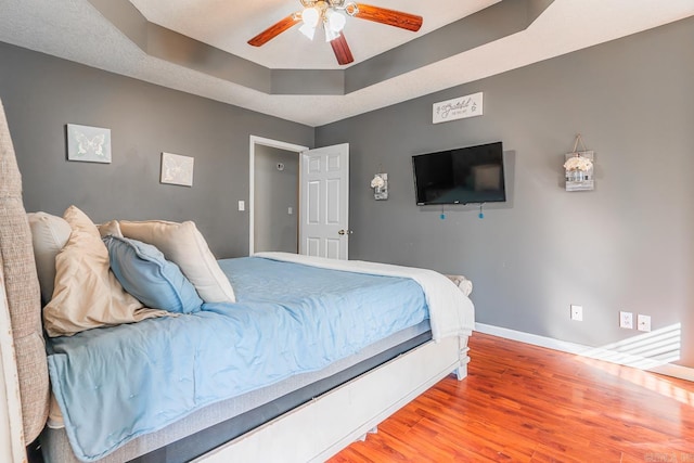 bedroom with a ceiling fan, a raised ceiling, baseboards, and wood finished floors