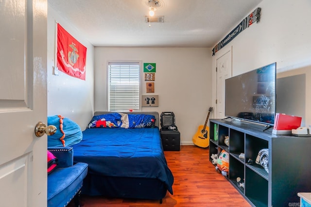 bedroom with a textured ceiling, wood finished floors, and visible vents