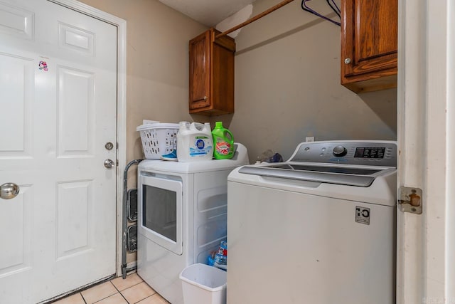 clothes washing area featuring light tile patterned floors, washer and clothes dryer, and cabinet space