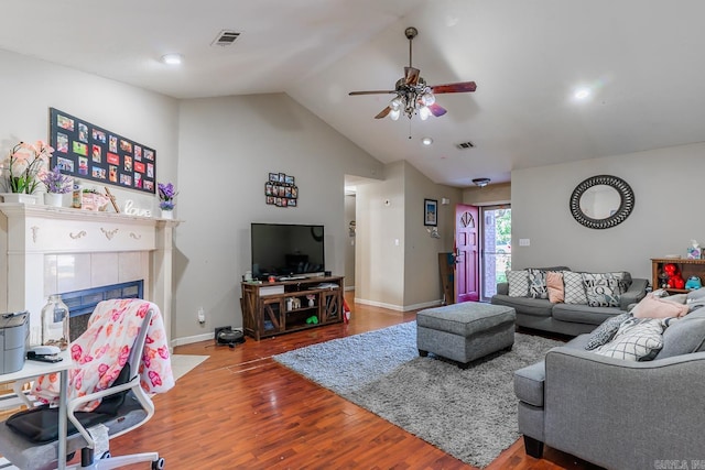 living area with vaulted ceiling, wood finished floors, a tile fireplace, and visible vents