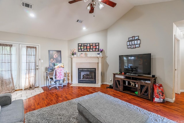 living area with lofted ceiling, visible vents, a tiled fireplace, and wood finished floors