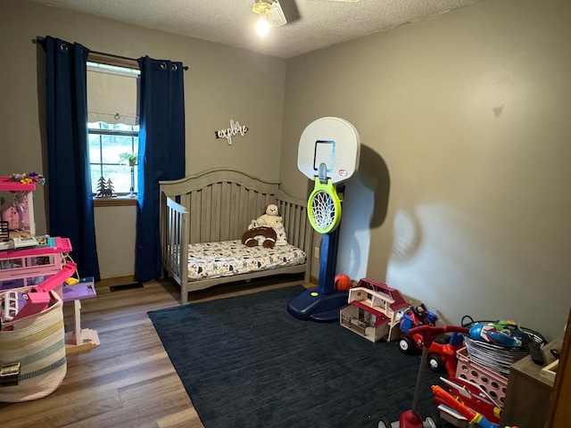 bedroom with a textured ceiling, a nursery area, and hardwood / wood-style flooring