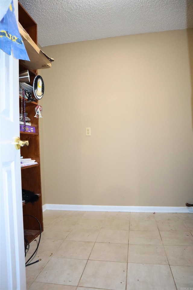 interior space featuring baseboards, a textured ceiling, and light tile patterned flooring