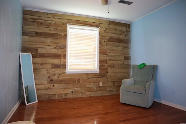 living area featuring visible vents, baseboards, wood finished floors, crown molding, and wood walls