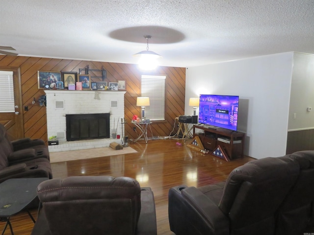 living room with wooden walls, hardwood / wood-style flooring, a textured ceiling, and a brick fireplace