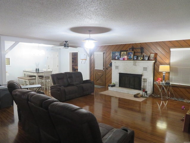 living room featuring dark wood-type flooring, wooden walls, a textured ceiling, a fireplace, and ceiling fan