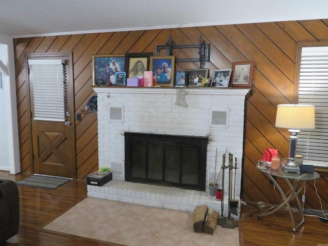 living room with wooden walls, a brick fireplace, and tile patterned flooring