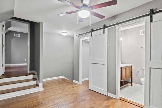 interior space with visible vents, a barn door, light wood-style floors, ceiling fan, and baseboards