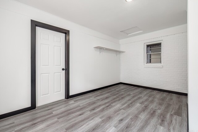 unfurnished room with brick wall and light hardwood / wood-style flooring