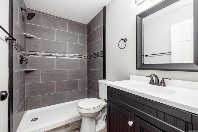 bathroom featuring vanity, toilet, wood-type flooring, and tiled shower