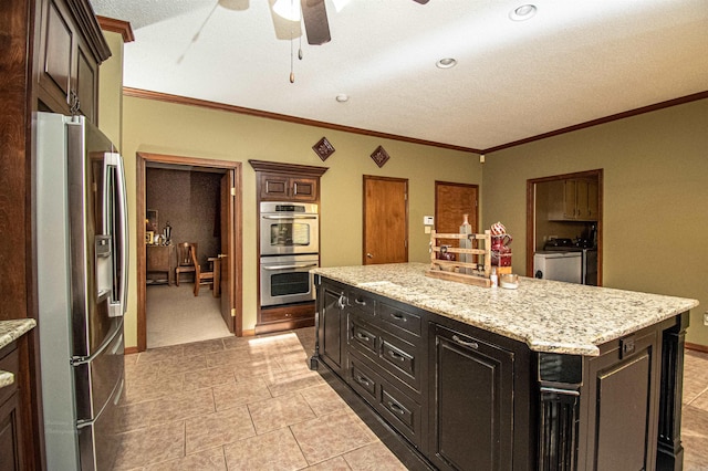 kitchen featuring baseboards, a kitchen island, appliances with stainless steel finishes, ornamental molding, and washing machine and dryer