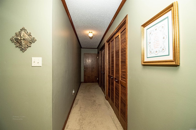 hallway with ornamental molding, light colored carpet, a textured ceiling, and baseboards