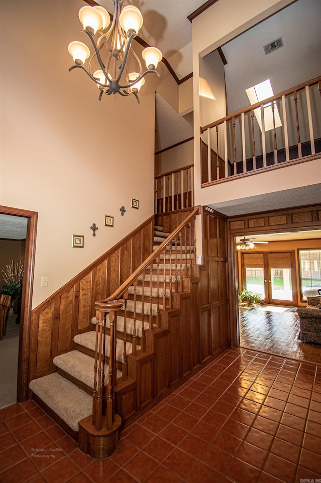 stairway with visible vents, a towering ceiling, an inviting chandelier, wainscoting, and wooden walls