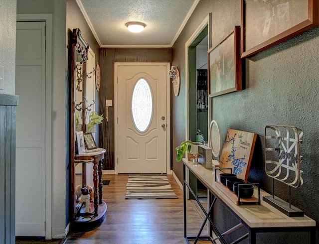 entryway with a textured ceiling, a textured wall, wood finished floors, baseboards, and ornamental molding