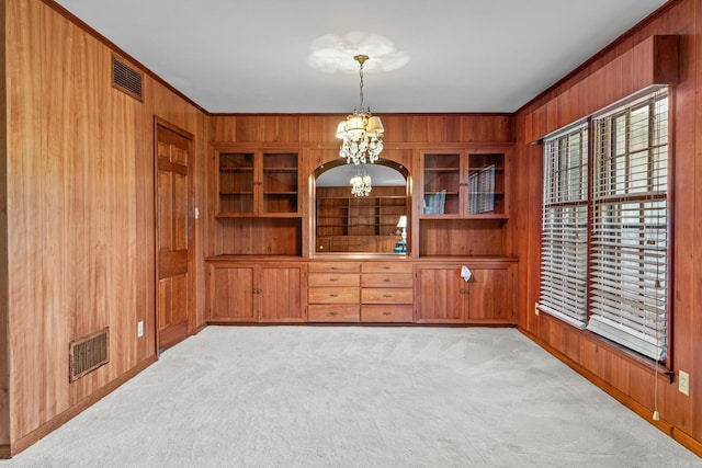 carpeted spare room featuring built in shelves, an inviting chandelier, wooden walls, and crown molding