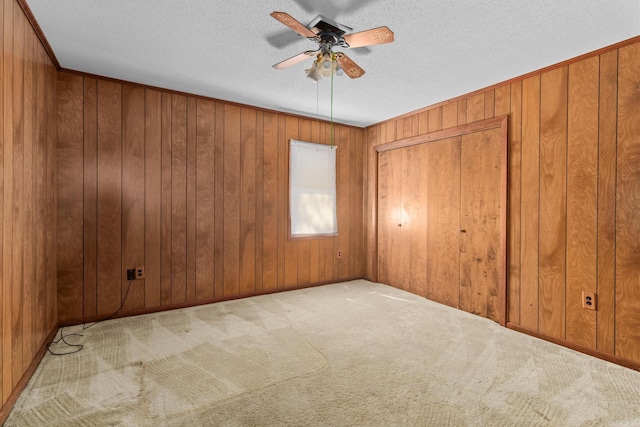 carpeted empty room with wooden walls, ceiling fan, and a textured ceiling