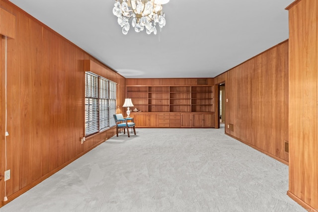 unfurnished room featuring wooden walls, crown molding, built in features, a chandelier, and light colored carpet