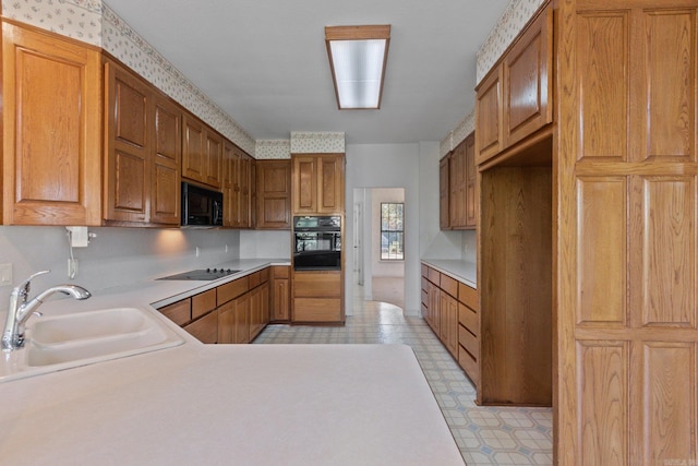 kitchen with light countertops, black appliances, brown cabinets, light floors, and a sink