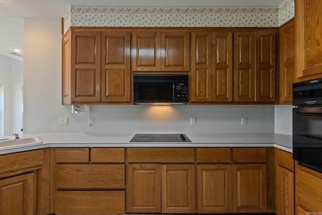 kitchen with a sink, light countertops, brown cabinetry, black appliances, and wallpapered walls