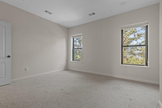 empty room with carpet, visible vents, and baseboards
