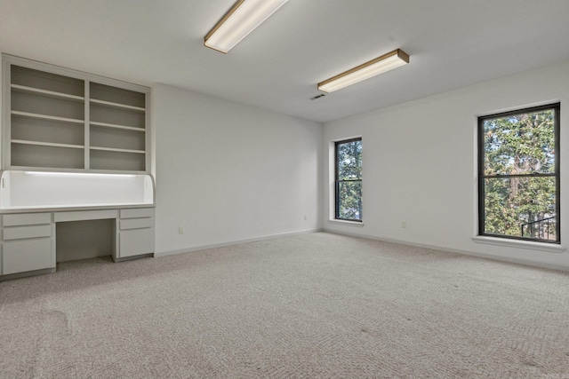 empty room with visible vents, built in study area, light colored carpet, and baseboards