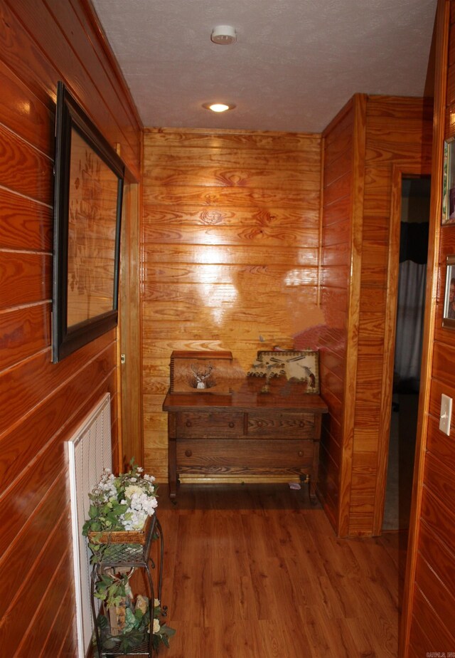 hallway with dark wood-type flooring, a textured ceiling, and wood walls