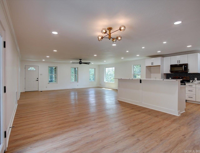 kitchen with white cabinets, ceiling fan with notable chandelier, light hardwood / wood-style flooring, decorative backsplash, and ornamental molding