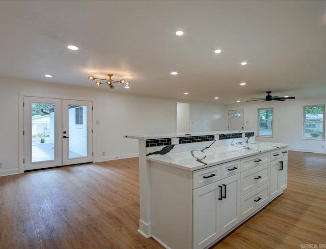 kitchen featuring white cabinets, light hardwood / wood-style floors, light stone counters, and ceiling fan