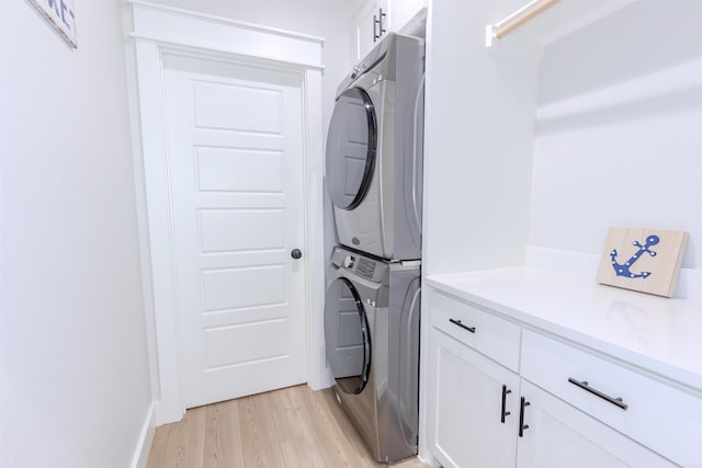 clothes washing area with light hardwood / wood-style floors, cabinets, and stacked washer / dryer