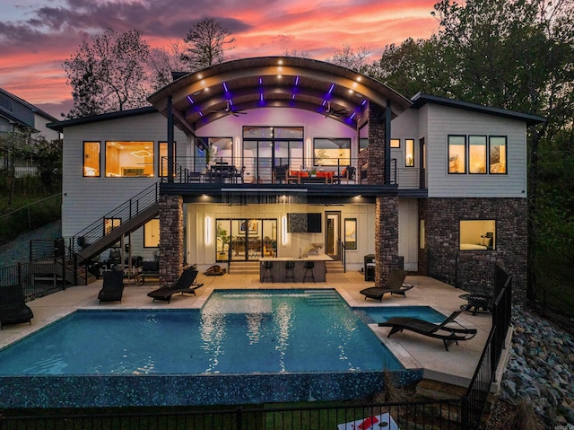 back house at dusk with a balcony and a patio