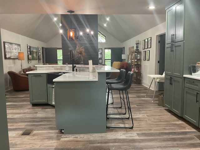 kitchen with lofted ceiling, wood-type flooring, a kitchen breakfast bar, pendant lighting, and a kitchen island with sink