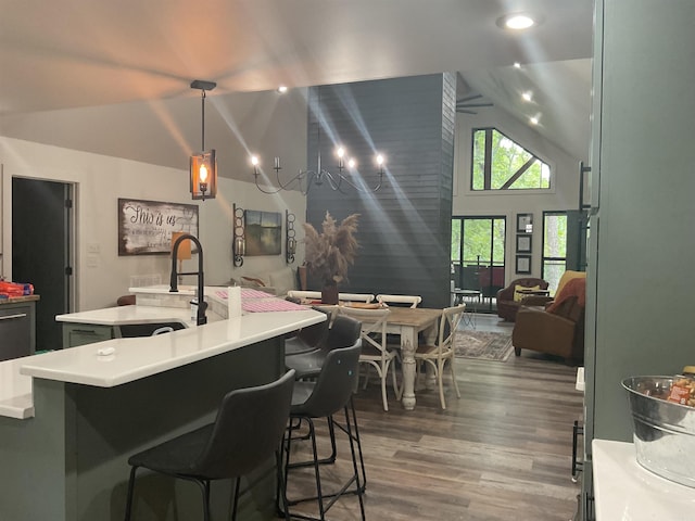 kitchen with dark hardwood / wood-style flooring, pendant lighting, a kitchen island with sink, high vaulted ceiling, and a chandelier