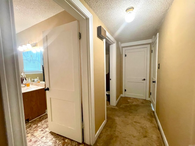 corridor with a textured ceiling and light carpet